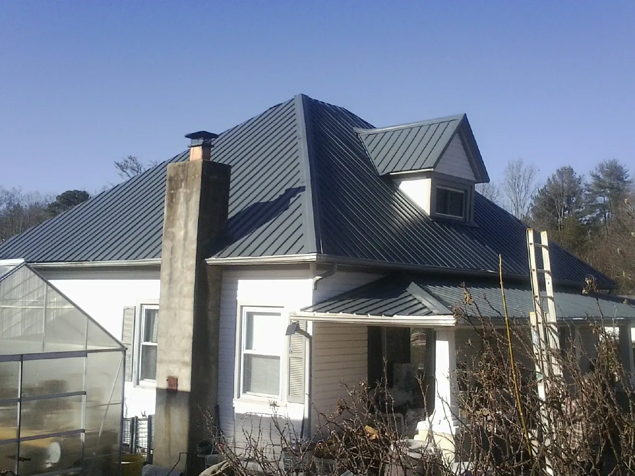 Dark blue standing seam metal roof on a white farmhouse with dormer — Slate & Tile Roof Repair by Roofing Brothers in Jacks Creek