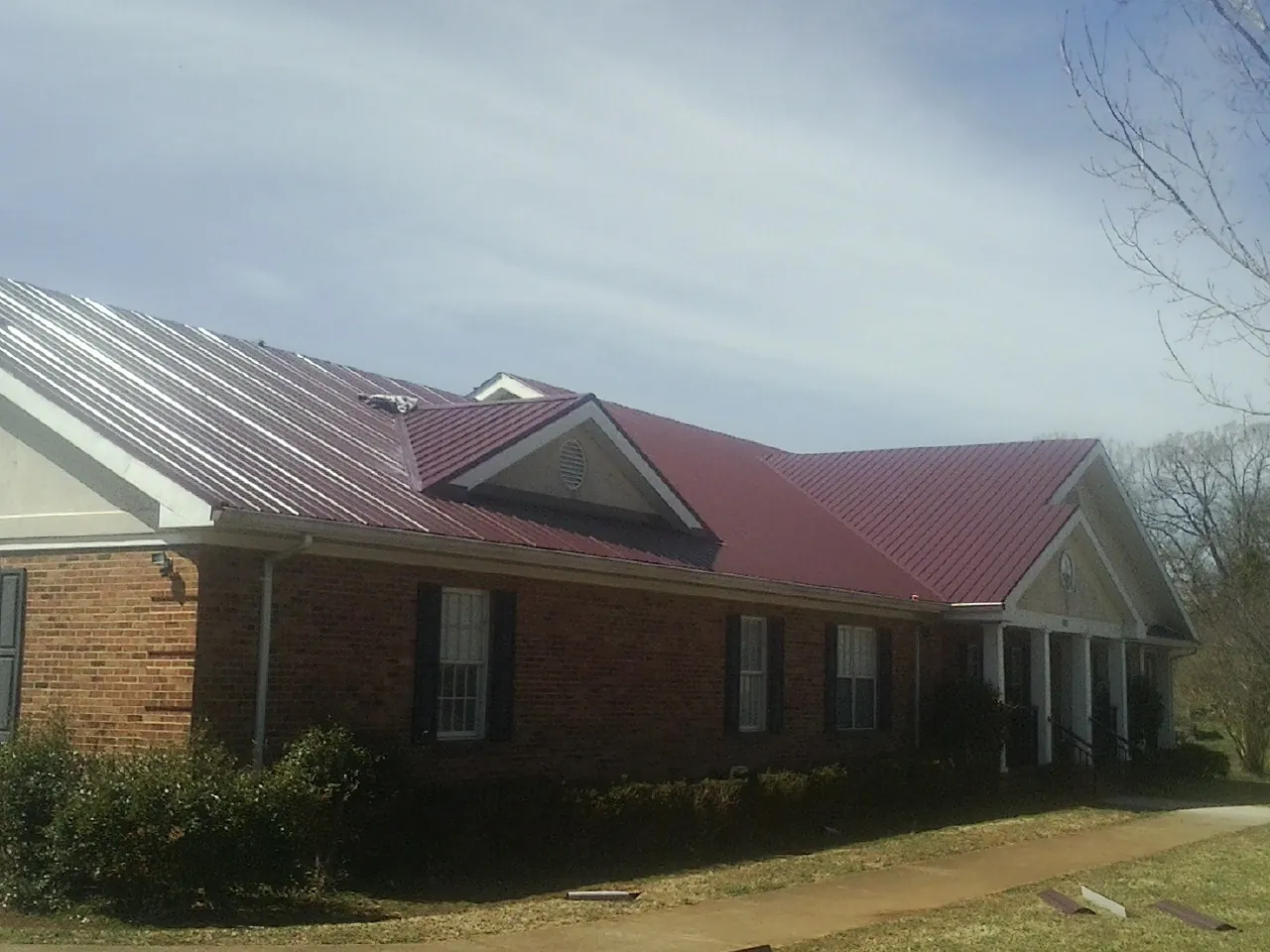 Red metal roof with gabled entries on a long brick building, from a Hail Damage Roof Repair job in Jacks Creek