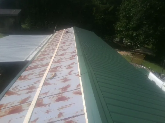 Old rusted panels beside newly installed green metal roofing — Wind Damage Roof Repair by Roofing Brothers in Jacks Creek