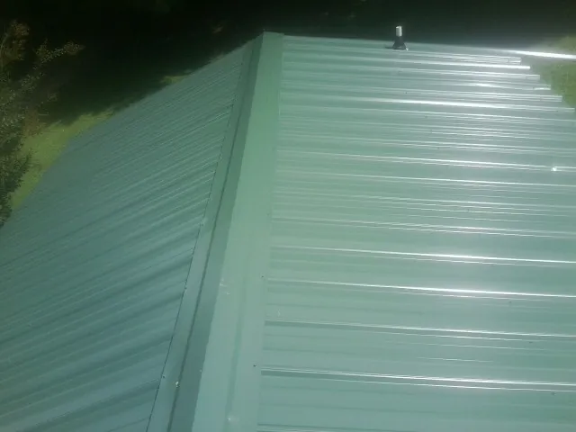 New green metal panels meeting at the ridge of a roof — Flat Roof Repair work by our crew in Jacks Creek