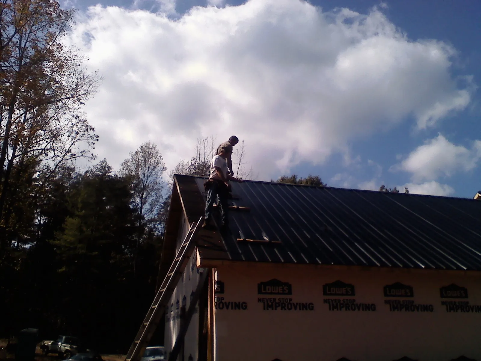 Roofer fastening dark metal panels high against a cloudy sky, from a Roof Inspection job in Jacks Creek