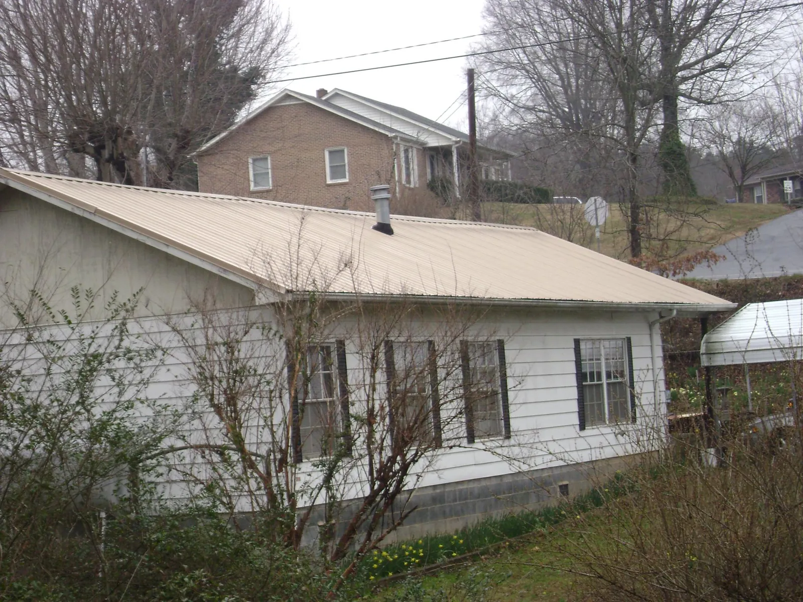 Tan metal roof on a white sided house set into a hillside — Commercial Roofing by Roofing Brothers in Jacks Creek